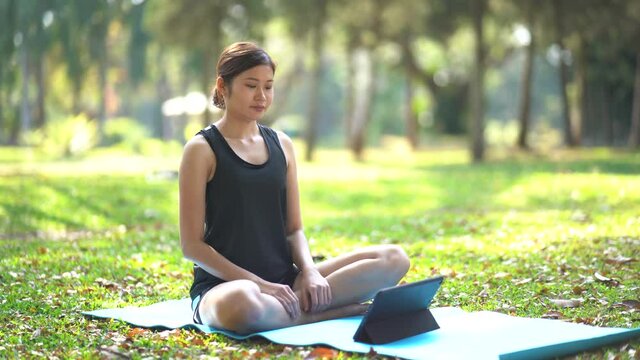 Young woman learning yoga exercise on a video conference outdoor in the park, sport yoga concept