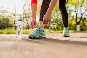 close-up feet of young attractive slim woman lacing shoelaces of sneakers doing sport exercises in morning sunrise jogging in park in sports wear, healthy lifestyle, water bottle