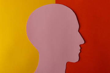 Head silhouette made of paper. Pink paper shaped as a human head with copy space on yellow and red paper background.