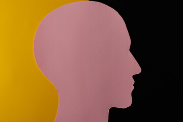 Head silhouette made of paper. Pink paper shaped as a human head with copy space on yellow and black paper background.