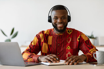 E-learning. Happy black man wearing headset study online with laptop at home