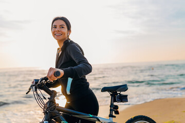 attractive slim woman riding bicycle, sport on morning sunrise beach in fitness suit, healthy...