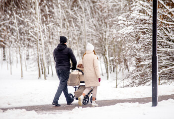 Fototapeta na wymiar A married couple rolls a child in a wheelchair in the winter Park 