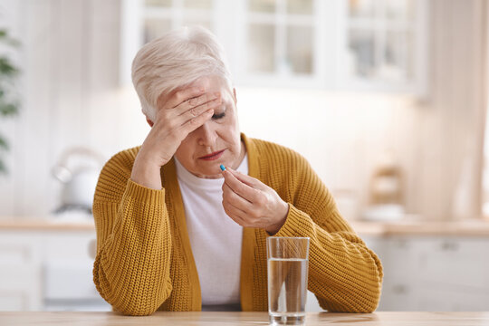 Old woman suffering from headache, taking pill