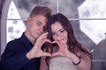 Valentine's Day. Love story. Young couple in love with hands making heart, Valentine Couple. Portrait of Smiling Beauty Girl and her Handsome Boyfriend making shape of Heart by their Hands. 