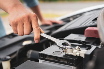 The hands of a skilled mechanic are holding a wrench to tighten a new car battery replacement nut,...