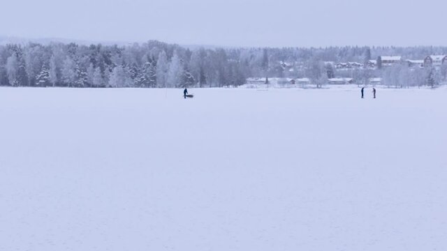 three people on a frozen lake including one person on a sled