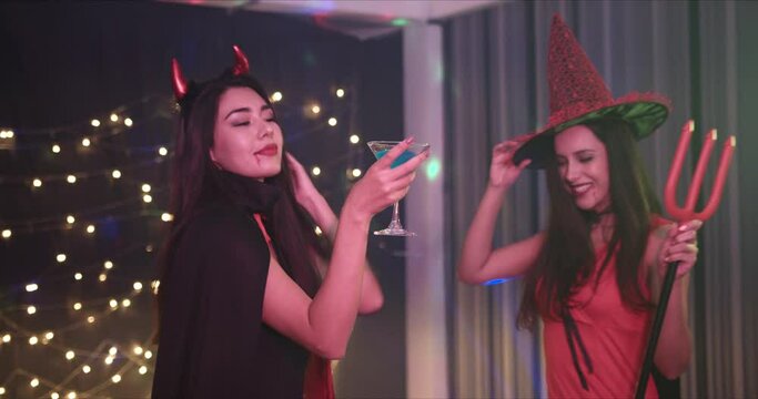 Medium Shot, Handheld - Two beautiful seductive young Caucasian female friends dressing in she devils seductively dancing at a Halloween costume party.