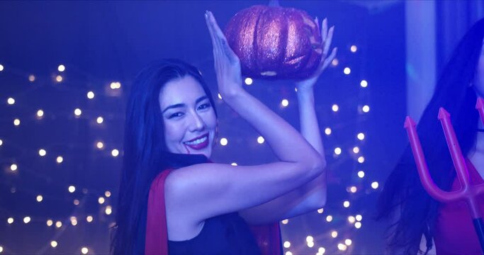 Close-up, Handheld - A young beautiful seductive Caucasian lady dressing in red she devil, holding a Halloween pumpkin in hand, dancing and enjoying a Halloween costume party.