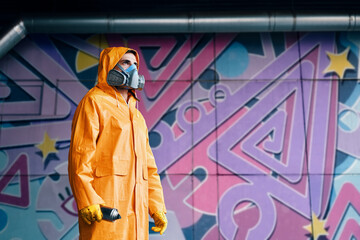 Graffiti painter in respirator mask standing near the wall with his paintings