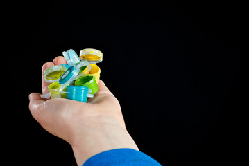 The boy holds multicolored paints in his hand. Hand close up isolated on black background.