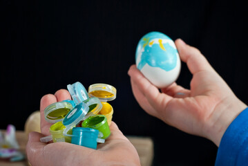 The boy paints an Easter egg. White egg in hand close up on a black background.
