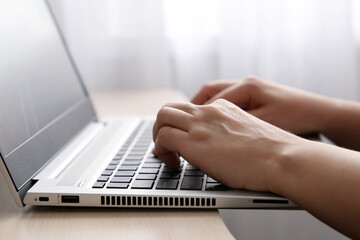 Female hands on laptop keyboard on a desk in sunlight. Woman types on the laptop keyboard sitting near the window, office or home work