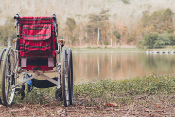 The wheelchair in the outdoor nature park, Autumn background, Concept of tourism for the disabled person, Relaxing among the water lake and beautiful natural, Have a good quality of disabilities life.