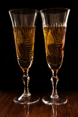 A pair of filled wine glasses on a black background. The glasses stand on a dark wood base.