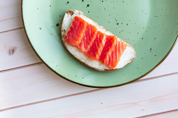 Toast with cream cheese, red fish salmon on a green ceramic plate on a white wooden background, breakfast