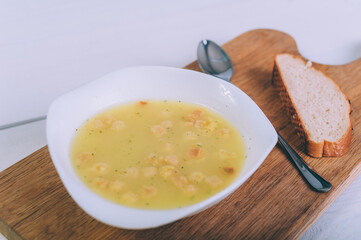 Soup broth in a bowl with bread on a wooden table.