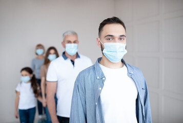 Young guy in medical mask standing in line for coronavirus immunization at health centre, empty space