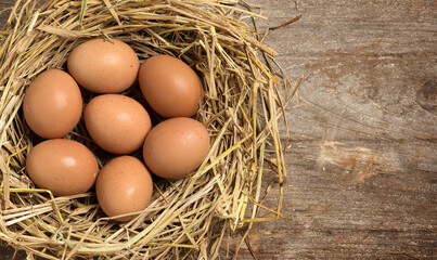 Top view fresh eggs on nest on old wooden background.