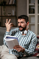 Fototapeta premium Man at home studying. Young man reading a book on the couch.