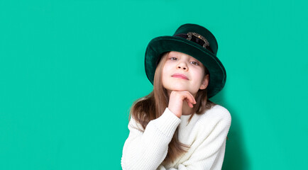 A closeup portrait of preteen girl in St. Patrick's Day hat on green backgroundwhite. Copy space