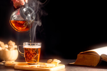 Man's hand pouring hot ginger tea in glass cup with water vapor. Organic Herbal Drink for Healthy