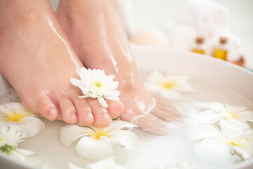 Obraz na płótnie Canvas closeup view of woman soaking her feet in dish with water and flowers on wooden floor. Spa treatment and product for female feet and hand spa. white flowers in ceramic bowl.