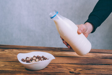 A man pours milk into cornflakes on a wooden background.