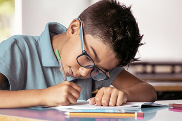 Focused Latin boy in glasses sitting at school desk and writing in copybook. Education or back to...