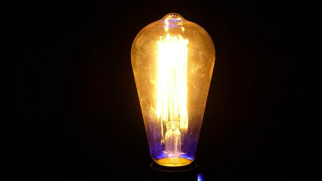 Retro vintage Edison light bulb flickers and turns on against black background.