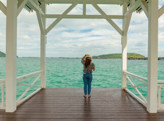Lady stand in seaside and hold her hand on hat and look out sea space