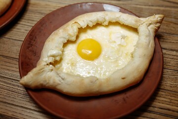 Top view on traditional Adjarian Khachapuri - open baked pie with melted salt cheese suluguni and egg yolk on wooden tray. Traditional georgian food
