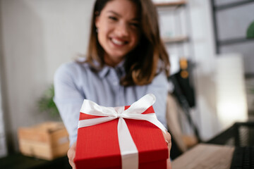 Portrait of a cheerful young businesswoman with gift. Happy businesswoman holding gift box