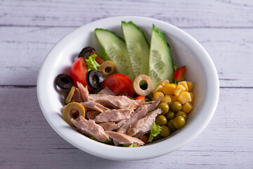 canned tuna salad with fresh vegetables in white plate on wooden background top view