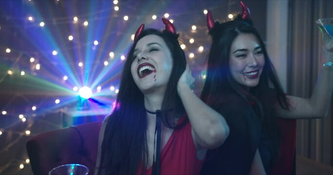 Medium Shot, Handheld - Two beautiful seductive young Caucasian female friends dressing in she devils seductively dancing at a Halloween costume party in a dark room with decorative lights. 
