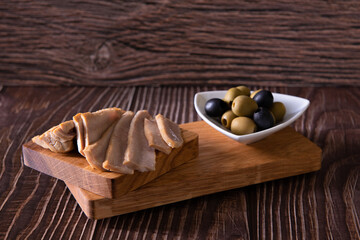 Fototapeta na wymiar tuna slices with olives on cutting board on wooden background closeup