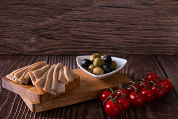 tuna slices with tomatoes and olives on cutting board on wooden background closeup