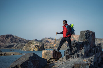 Young indian traveler standing confidently on top of the mountain over a cliff, wearing a red snow jacket. Confident and success concept.