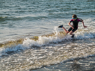 Teenager girl in dark wet suit and shoes jumping in the ocean, West coast of Ireland, Atlantic ocean. Outdoor activity concept