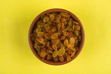 Raisins in a bowl on a yellow background.