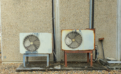 Two old air conditioner compressors on wall outside the house