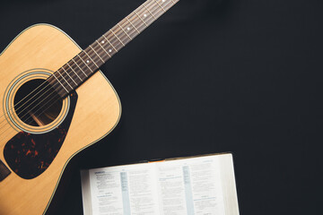 Fototapeta na wymiar A guitar and an open bible on a black background