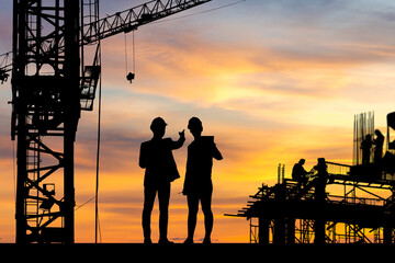 Naklejka premium Silhouette of Engineer and worker checking project at building site background, construction site at sunset in evening time.