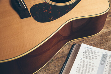 Side view of a guitar and a bible on a wooden background in a dimly lit environment. Soft light and...