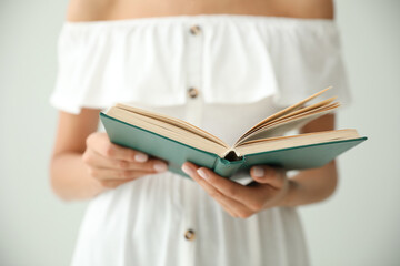 Young woman reading book on light grey background, closeup