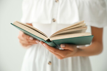 Young woman reading book on light grey background, closeup
