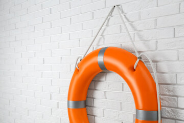 Orange lifebuoy and space for text on white brick wall. Rescue equipment