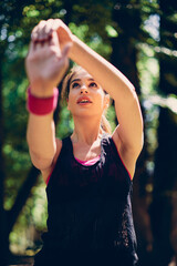 Low angle view of sportswoman stretching her arms in nature. She is doing warm up exercises.
