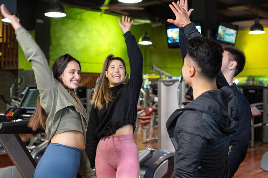 Happy diverse group of friends, high five celebrating, enjoying fitness workout together in gym. High quality photo.