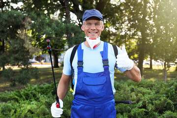 Worker with insecticide sprayer near green bush outdoors. Pest control
